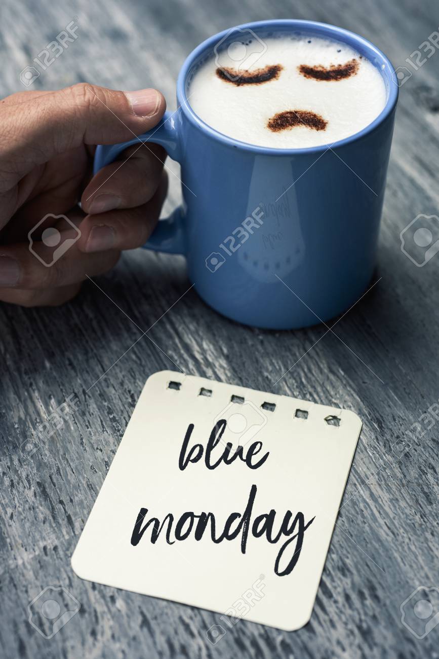 closeup of a note with the text blue Monday written in it on a gray rustic table and a young caucasian man with a blue cup of cappuccino with a sad face drawn with cocoa powder on its milk foam - 92990910 closeup of a note with the text blue Monday written in it on a gray rustic table and a young caucasian man with a blue cup of cappuccino with a sad face drawn with cocoa powder on its milk foam - 92990910