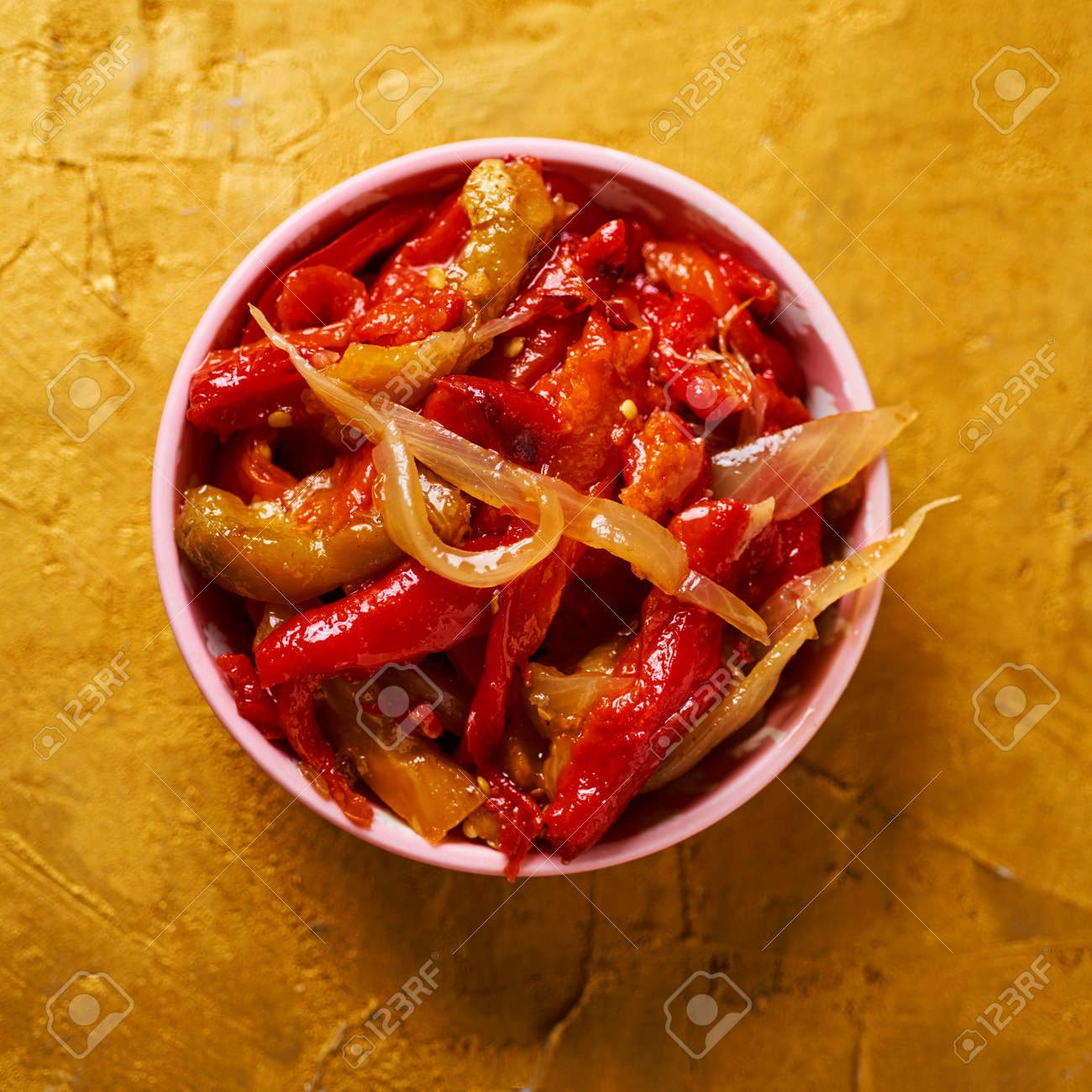 high angle view of a pink bowl with escalivada, a typical dish of Catalonia, Spain, made with grilled and peeled vegetables, on a golden textured surface - 155411776 high angle view of a pink bowl with escalivada, a typical dish of Catalonia, Spain, made with grilled and peeled vegetables, on a golden textured surface - 155411776