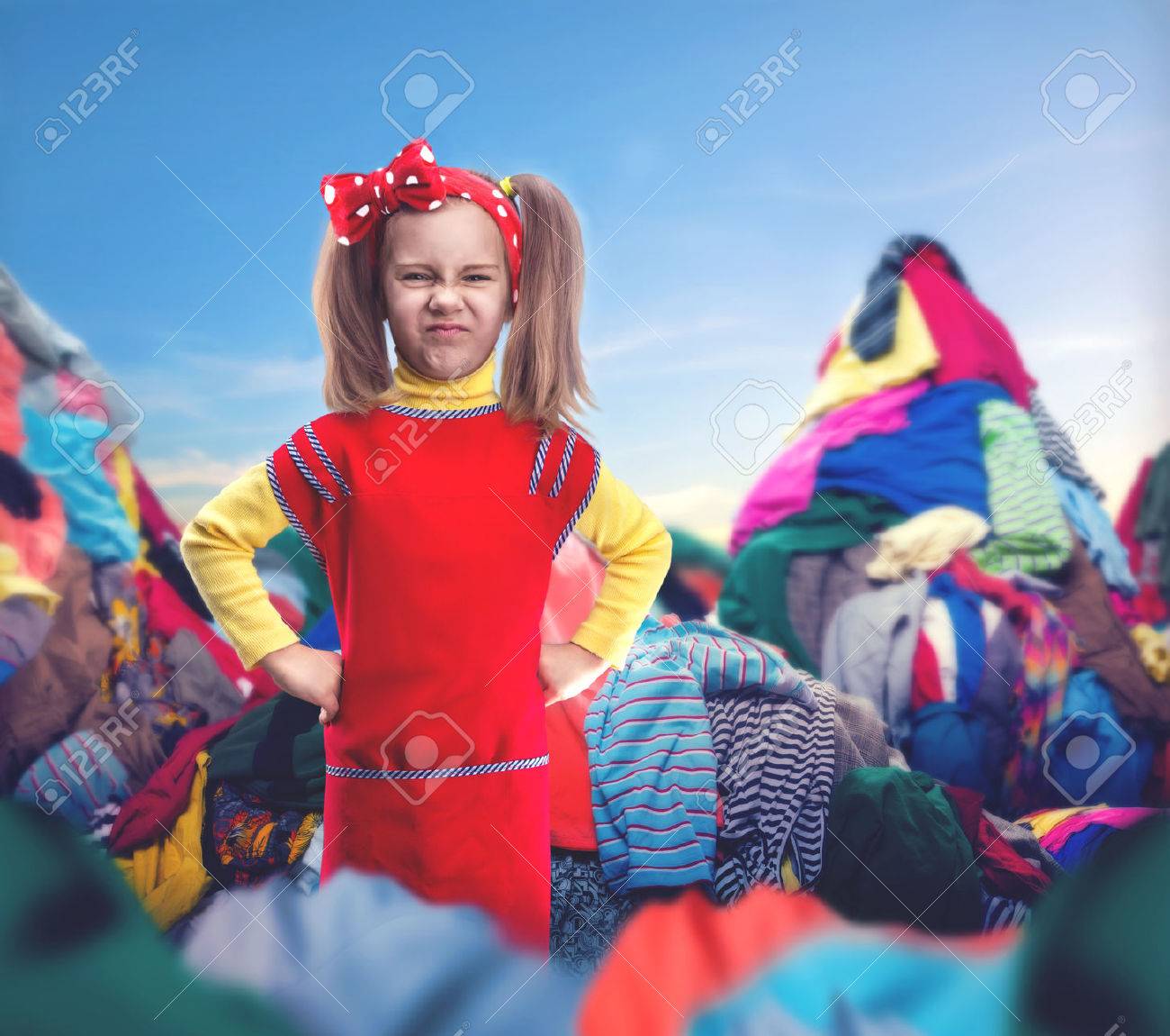 Little girl with her hands on hips stands among heaps of clothes - 44113244 Little girl with her hands on hips stands among heaps of clothes - 44113244