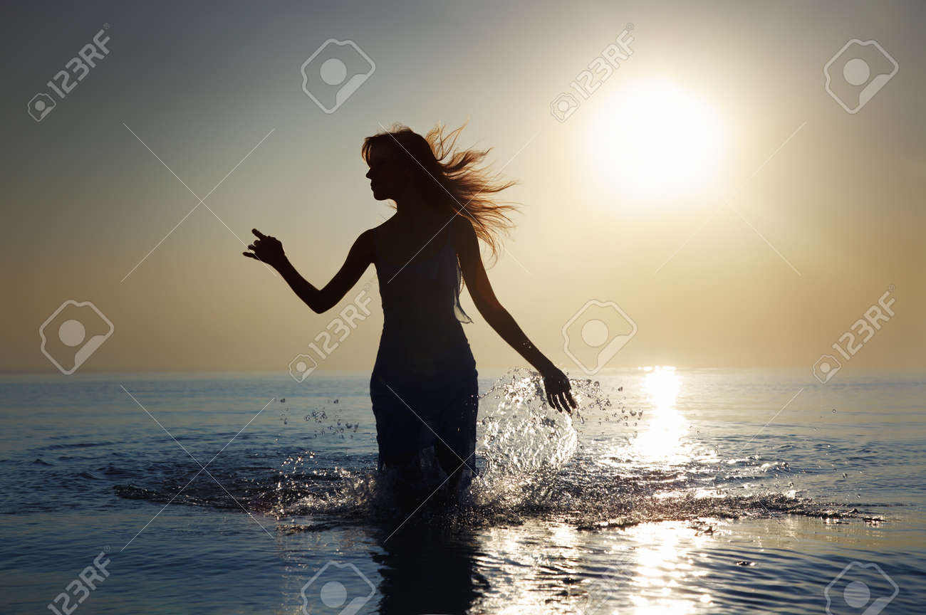 Silhouette of the woman with long hairs walking in the water during sunrise. Natural darkness and colors - 8908445 Silhouette of the woman with long hairs walking in the water during sunrise. Natural darkness and colors - 8908445