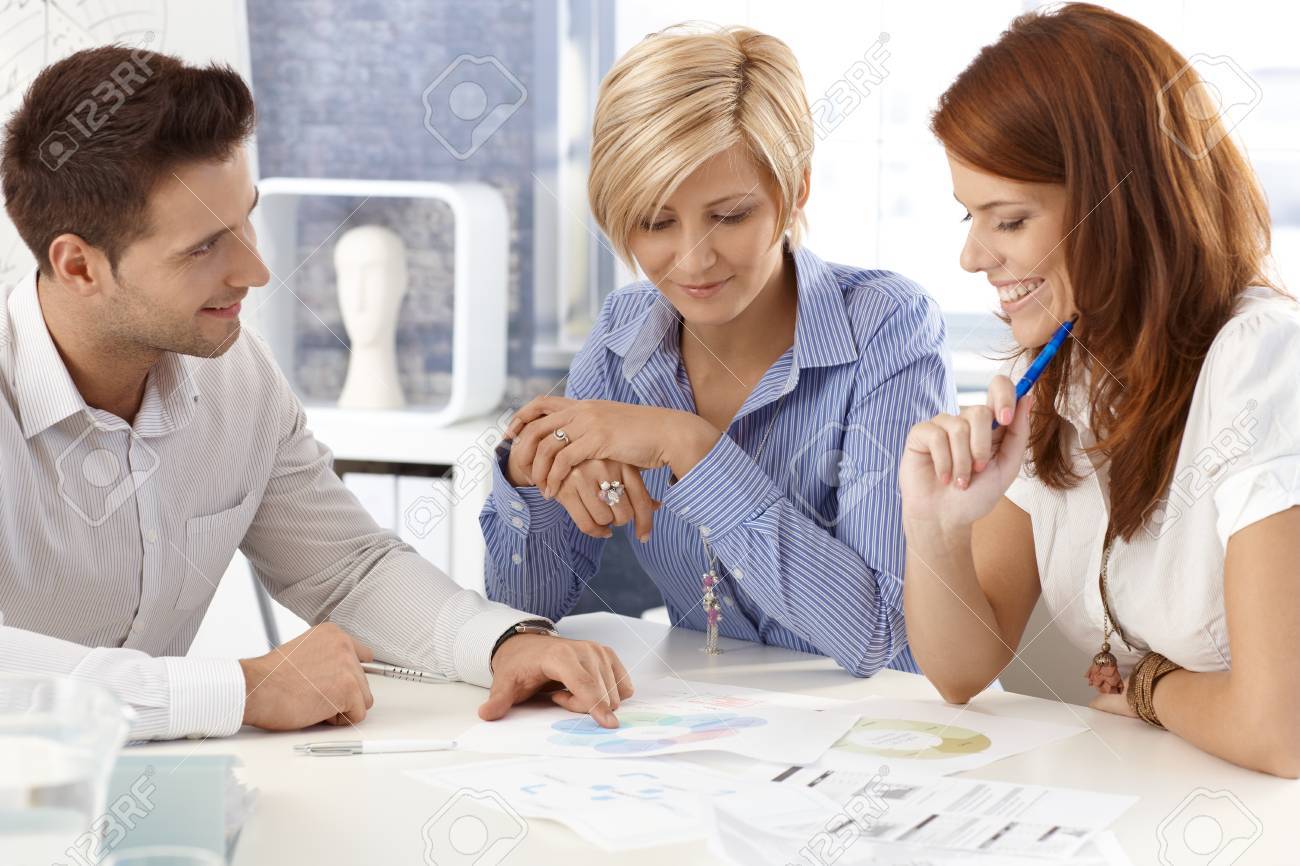 Portrait of happy businessteam working together a meeting table, businessman explaining, pointing at documents. - 12472059 Portrait of happy businessteam working together a meeting table, businessman explaining, pointing at documents. - 12472059