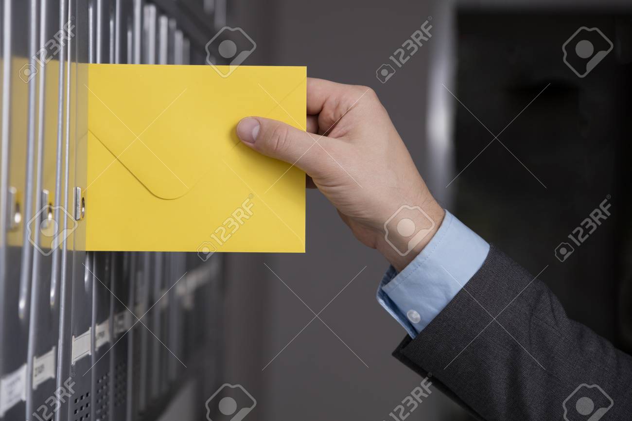 mailmanâ s hand putting the yellow envelope into the gray mailbox