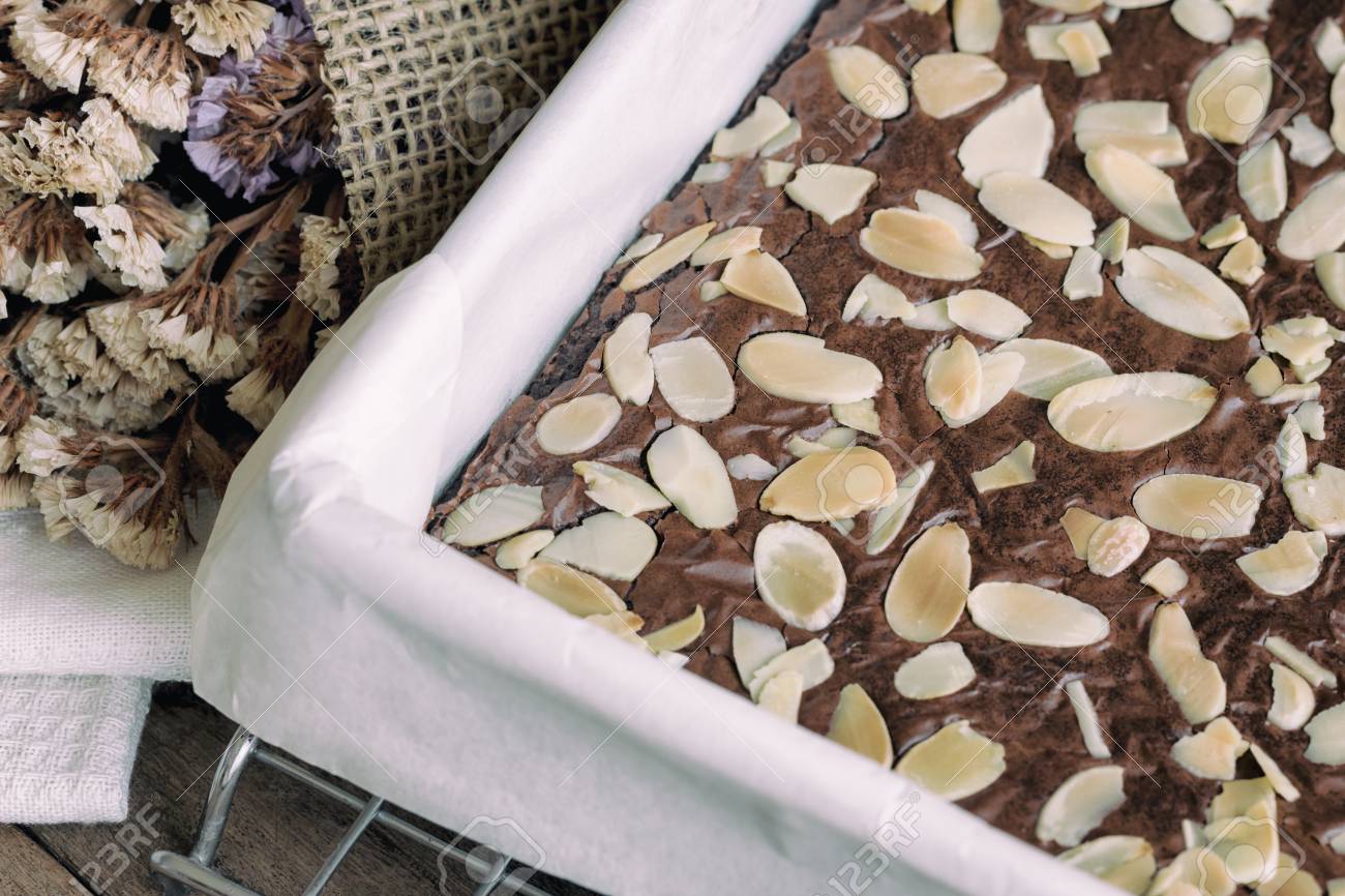 homemade dark chocolate brownies topping almond slices in square baking sheet cover