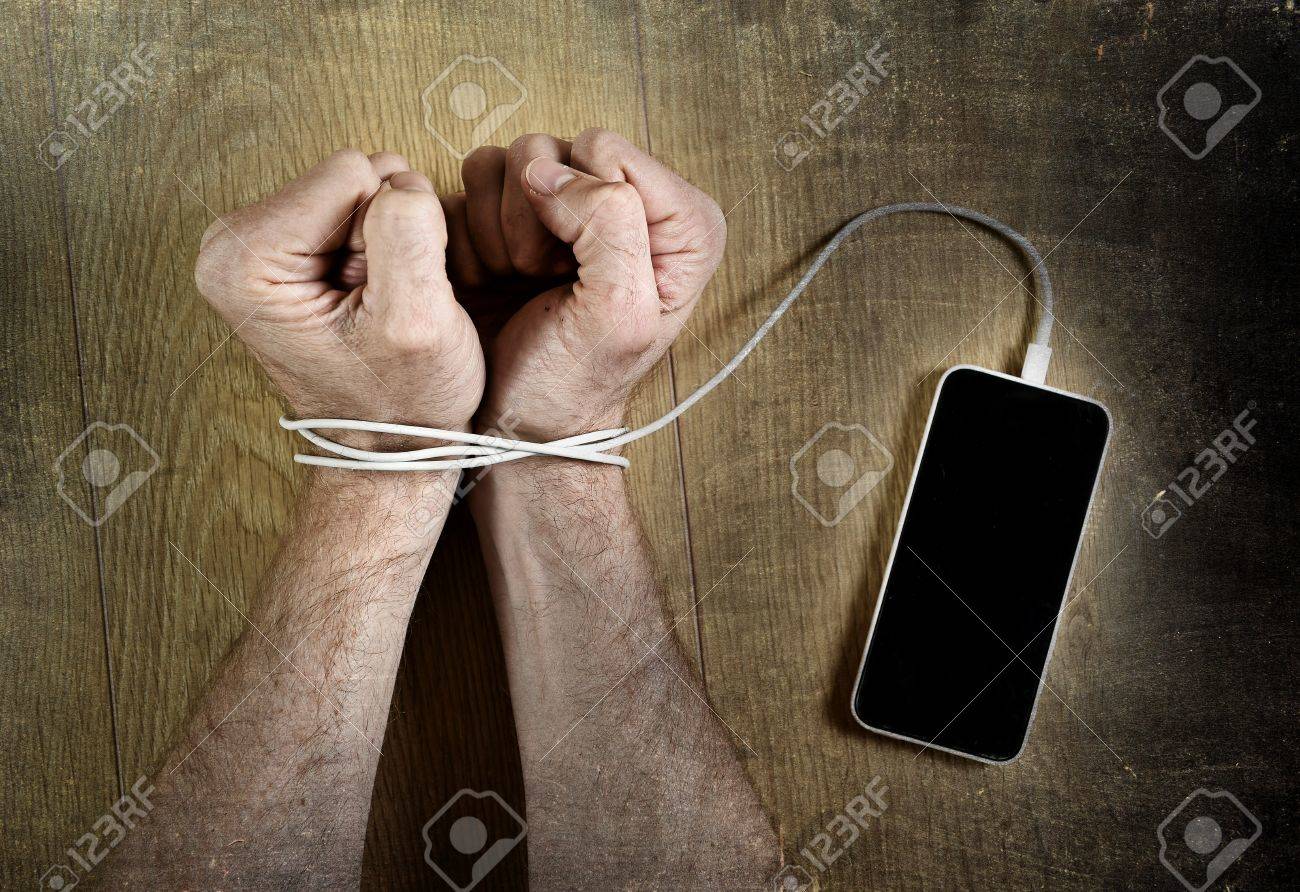 man hands trapped and wrapped on wrists with mobile phone cable as handcuffs in smart phone networking and communication technology addiction concept - 46987931 man hands trapped and wrapped on wrists with mobile phone cable as handcuffs in smart phone networking and communication technology addiction concept - 46987931