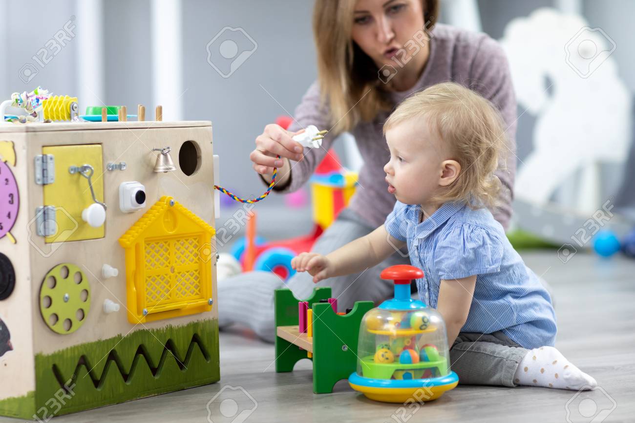 cute toddler baby playing with busyboard mother or babysitter kid babysitter