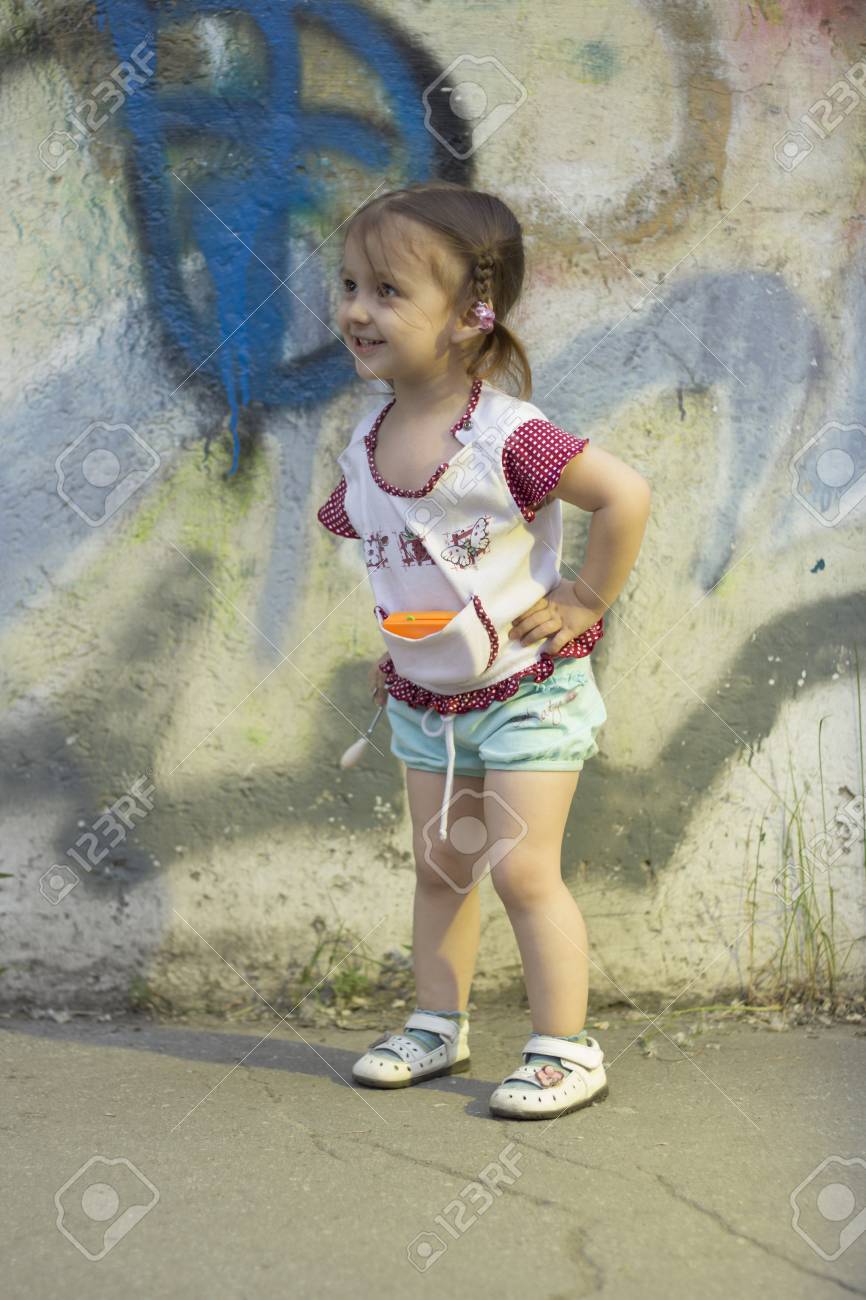 肯定的な子供たち 幸せ少女 2 3 4 歳彼女の頭の上のひもの略で 落書きでコンクリートの壁 女の子の手が彼女のお尻の近くの通りの笑顔します の写真素材 画像素材 Image