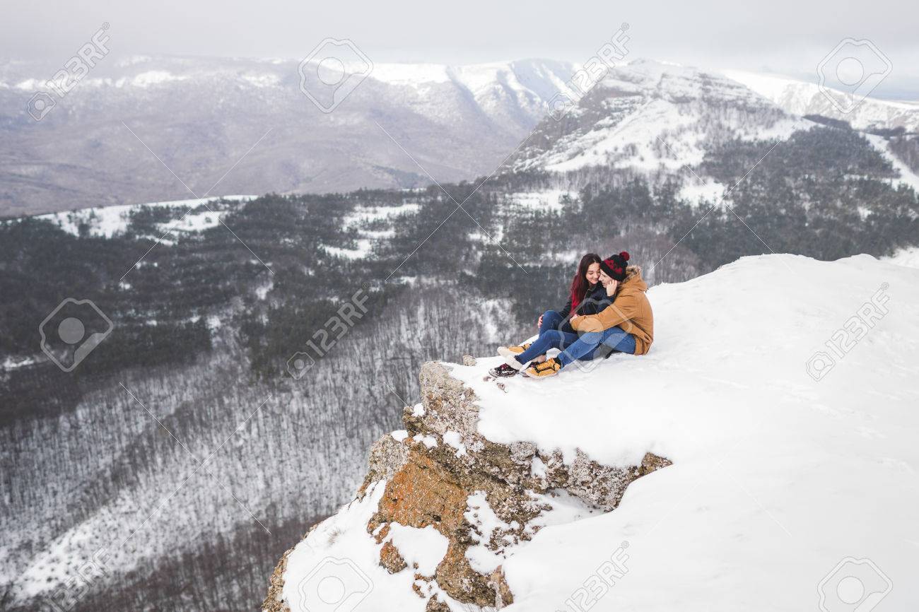 Couple Sitting On Edge Of Cliff In Mountains With Beautiful View Winter And Snow Stock Couple Sitting On Edge Of Cliff In Mountains With Beautiful View Winter And Snow Stock