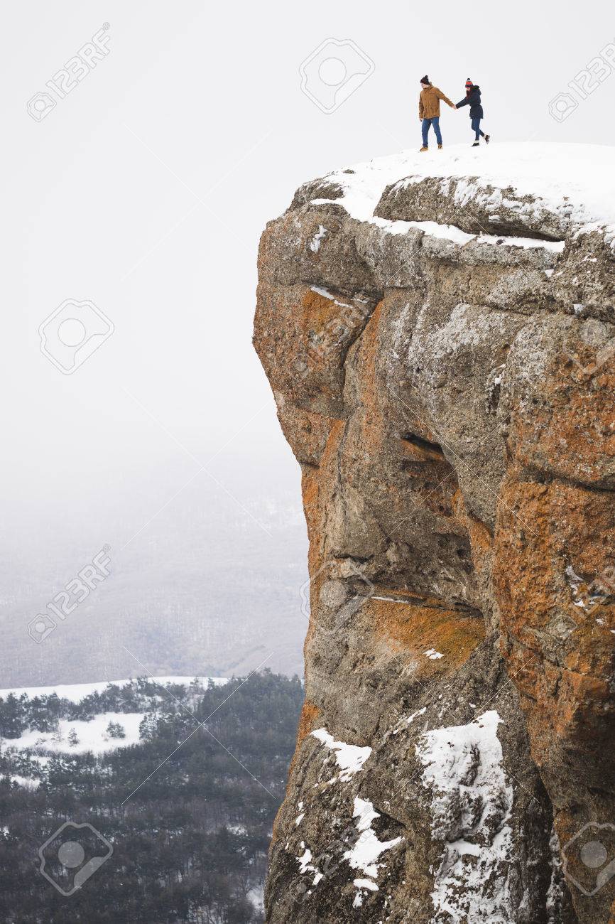People Standing On Edge Of Mountain Cliff Fog And Snow Around Stock Photo People Standing On Edge Of Mountain Cliff Fog And Snow Around Stock Photo