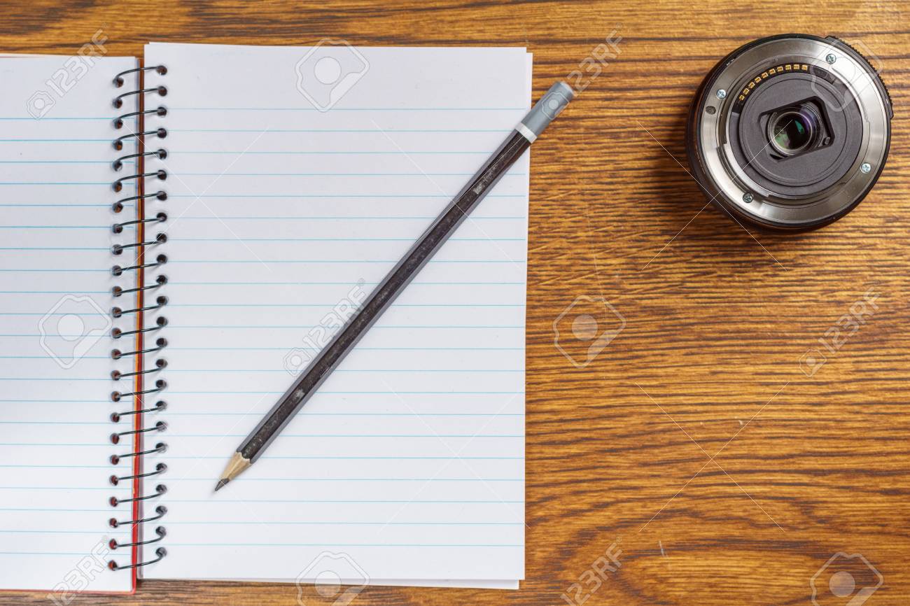 机の背景に黒い鉛筆とカメラレンズを備えたオープンスパイラルノートブックのトップビュー の写真素材 画像素材 Image 92739016
