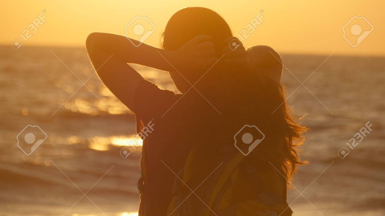 夕暮れ時 海の近くのビーチにポニーテールを結ぶ若い観光客女性 美しい少女は 日の出の海海岸で彼女の髪を絞る 女性バックパッカーの髪を編み 髪型 を作るします 髪のケア背面図 の写真素材 画像素材 Image