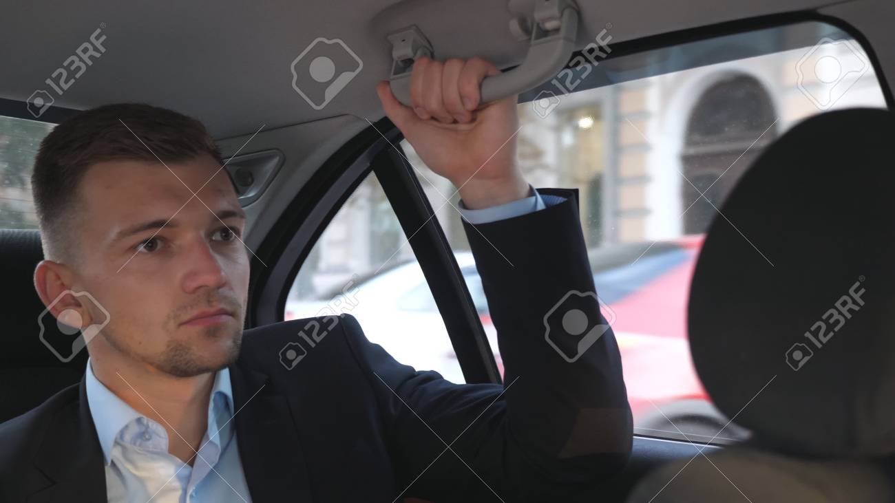 若いビジネスマンが車の後部座席に座って話をする 男はオートの後ろの席に座って話す タクシーの中を走行中の男は 運転手に何かを言って クローズアップスローモーション の写真素材 画像素材 Image