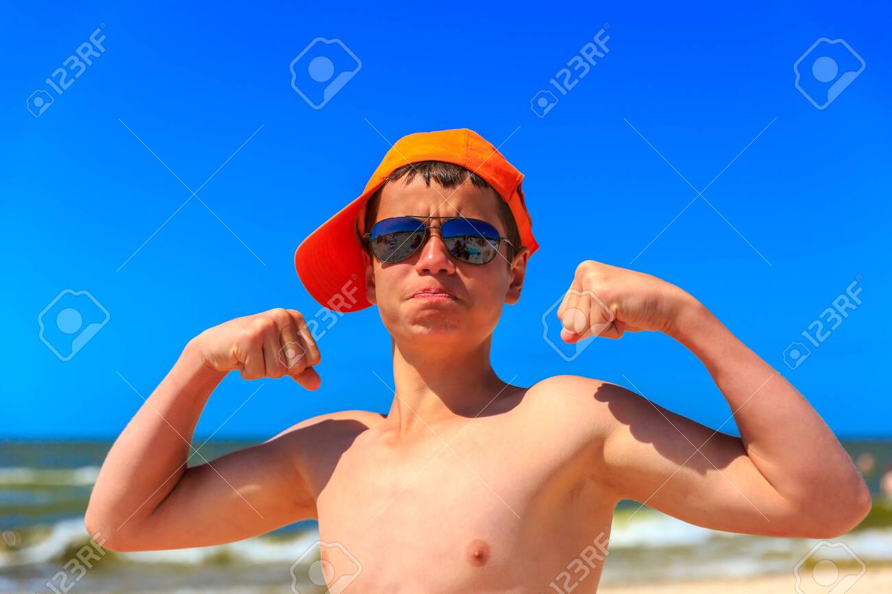 Muchacho Alegre Feliz De Trece Años La Playa De Mar Con Una Gorra Y Gafas De Sol Bíceps. Poca Profundidad De Campo, Se Centran En Las Manos Y La Cara