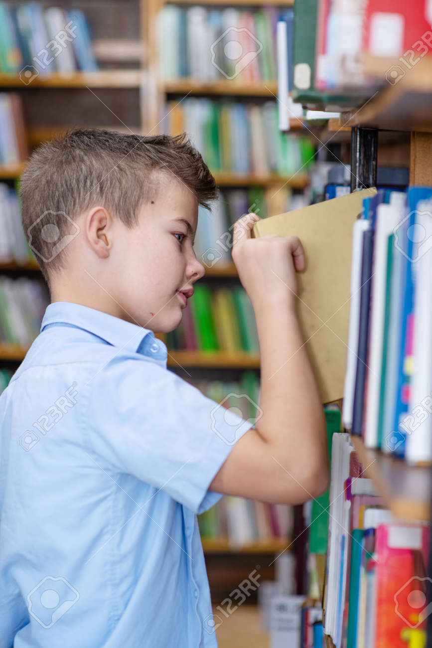 A boy in a blue shirt in a library takes a book from a bookshelf - 157471616 A boy in a blue shirt in a library takes a book from a bookshelf - 157471616