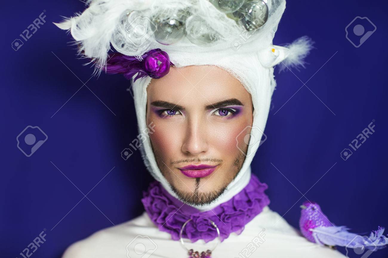 完璧なメイク男顔のクローズ アップの肖像画 明るい色 集中的な唇 ピンク白い影 長いまつ毛 創造的なドレス白紫鳥頭ピジョン メール上に座っています 新しいクレイジー アート ファッション の写真素材 画像素材 Image