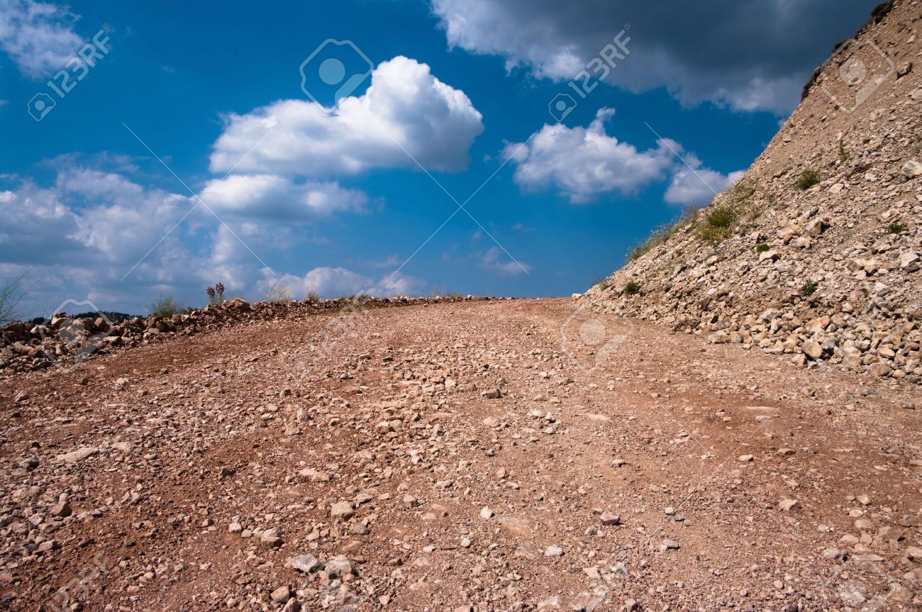 dirt road of rocky ground on background clouds in blue sky stock