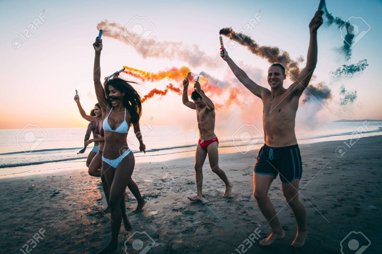 Group of friends having fun running on the beach with smoke bombs - 128421883 Group of friends having fun running on the beach with smoke bombs - 128421883
