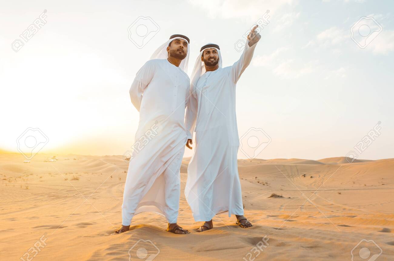 Two business men wearing traditional uae white kandura spending time in the desert of Dubai - 137877369 Two business men wearing traditional uae white kandura spending time in the desert of Dubai - 137877369