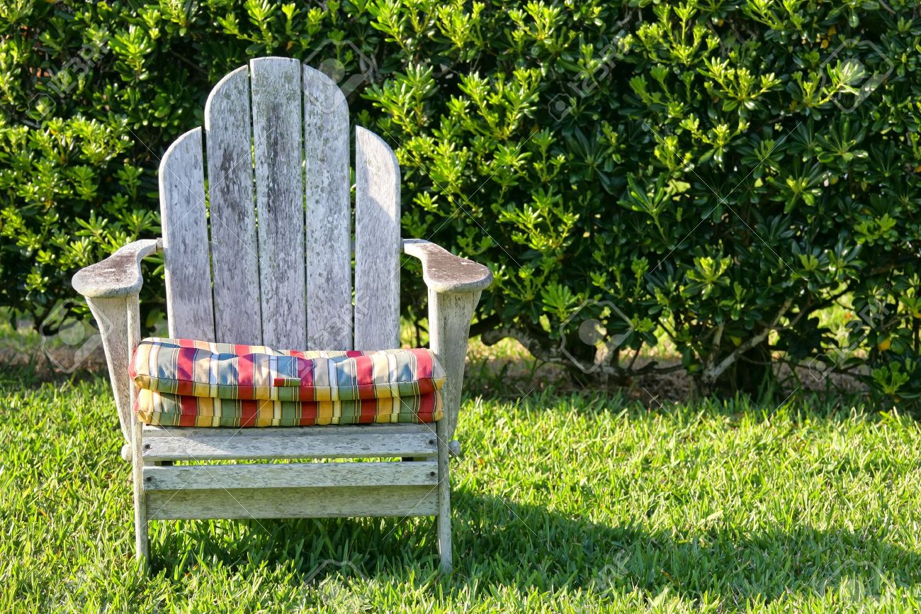 An Old Weathered Adirondack Chair In The Garden With A Hedge An Old Weathered Adirondack Chair In The Garden With A Hedge