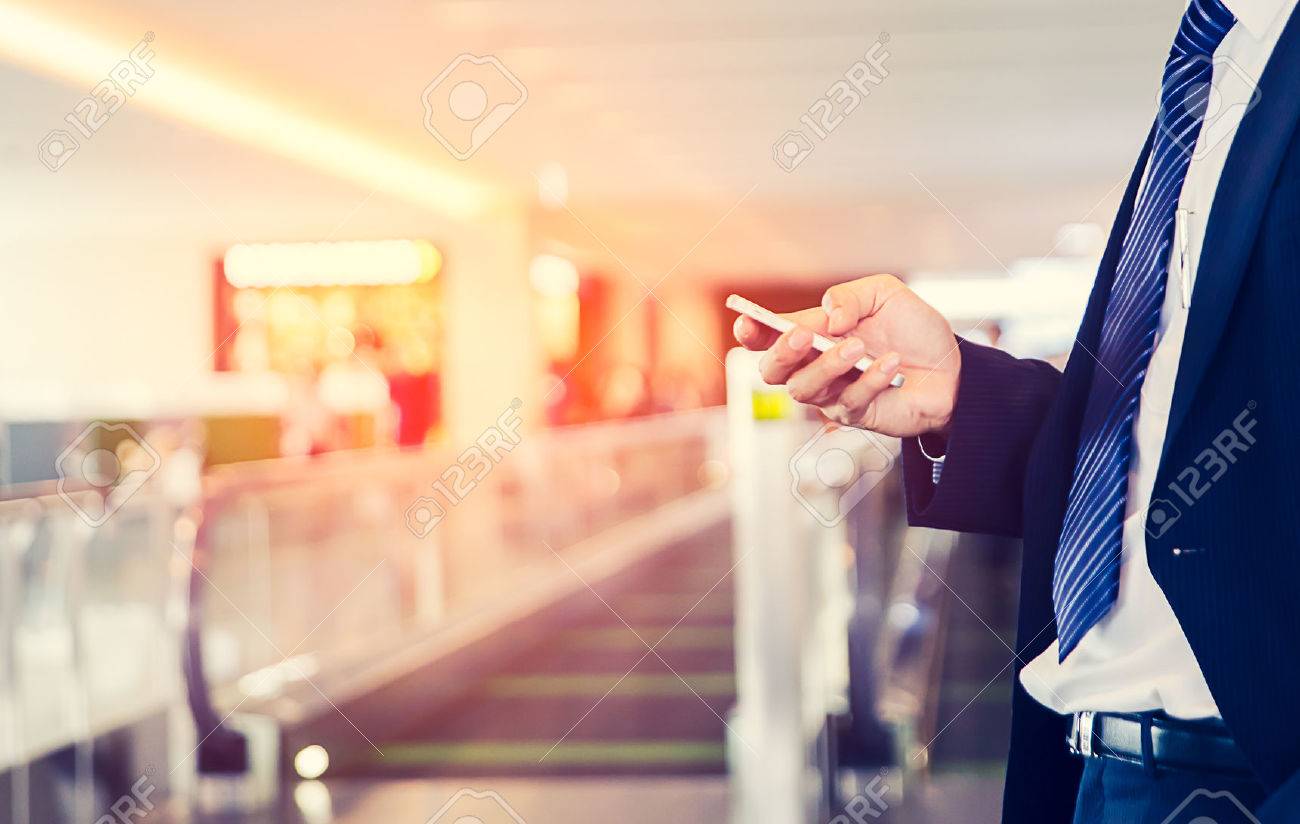 business man is Doing Business on mobile phone, while is sitting in Airport near window with sun rays during his business trip. - 67431583 business man is Doing Business on mobile phone, while is sitting in Airport near window with sun rays during his business trip. - 67431583