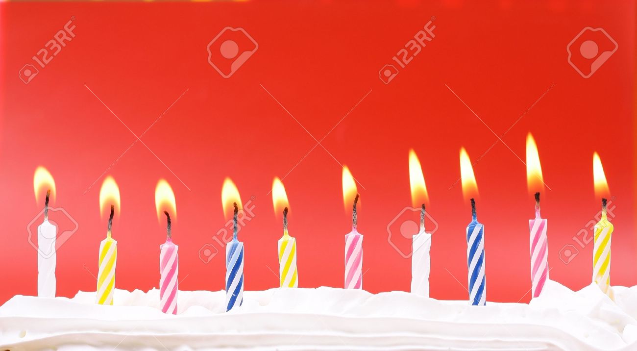 10 lit birthday candles in bright colors with red background stock