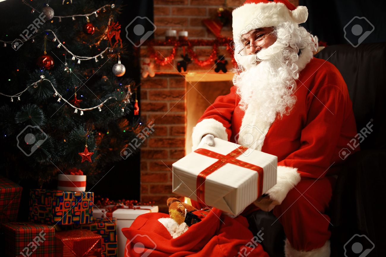 Santa Claus brought gifts for Christmas and having a rest by the fireplace. Home decoration. - 46918200 Santa Claus brought gifts for Christmas and having a rest by the fireplace. Home decoration. - 46918200