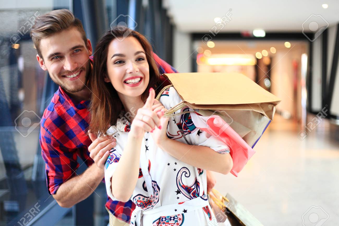 sale, consumerism and people concept - happy young couple with shopping bags walking in mall. - 94878214 sale, consumerism and people concept - happy young couple with shopping bags walking in mall. - 94878214