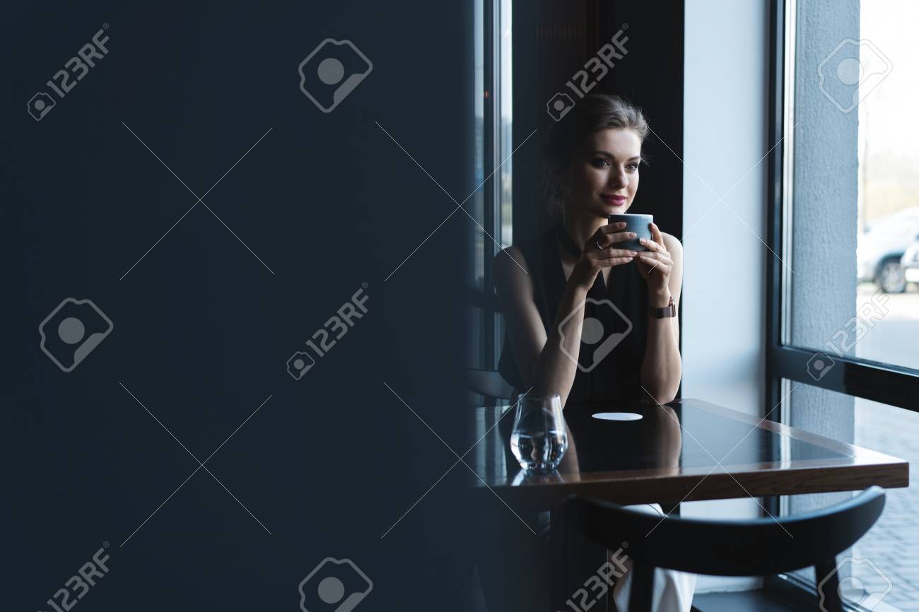 Portrait of gorgeous female drinking tea or coffee and looking with smile out of the coffee shop window while enjoying her leisure time - 124623163 Portrait of gorgeous female drinking tea or coffee and looking with smile out of the coffee shop window while enjoying her leisure time - 124623163