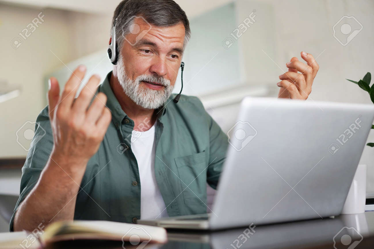 Attractive mature male remote working from home and having work confrence video call. - 171571091 Attractive mature male remote working from home and having work confrence video call. - 171571091