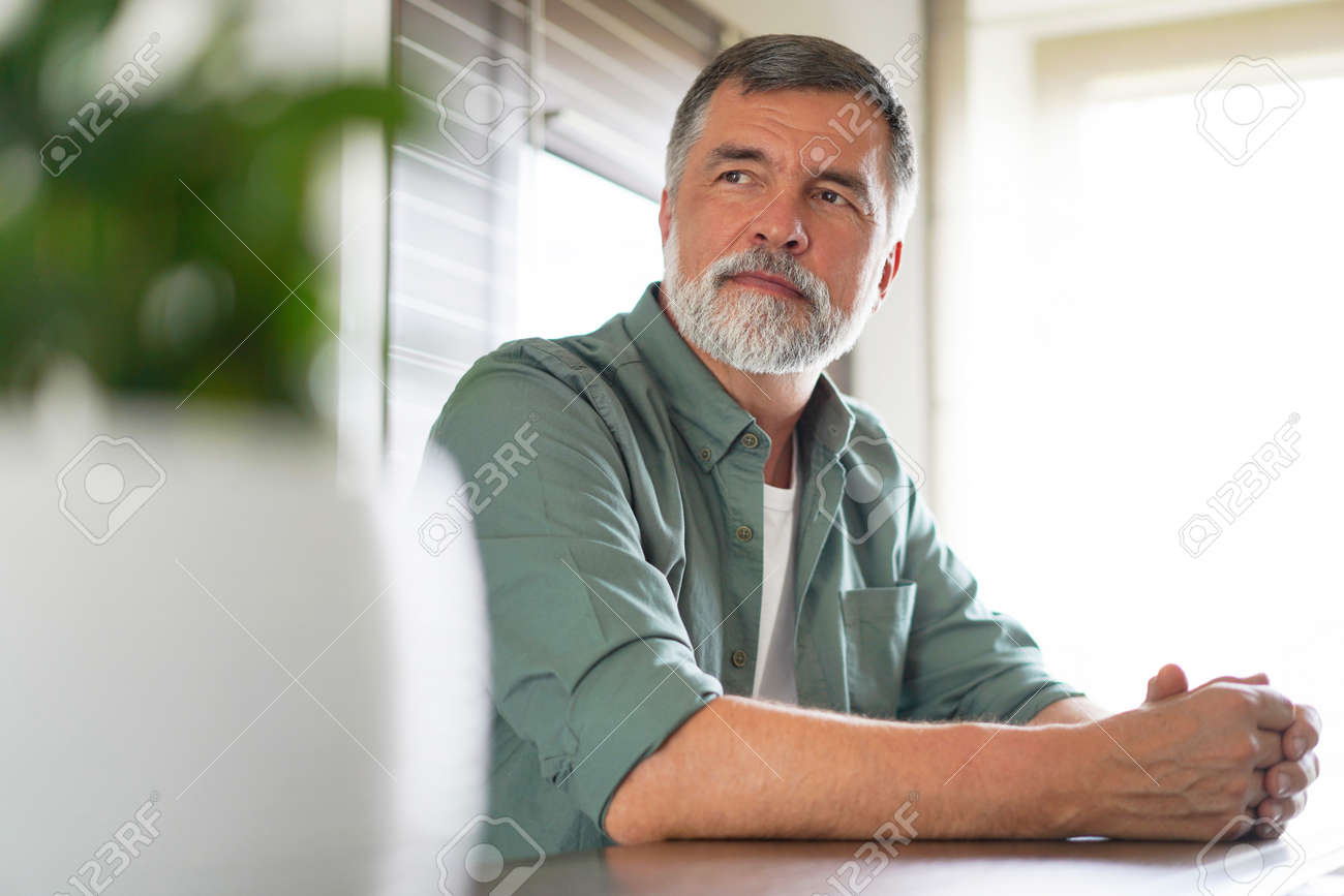 Happy attractive mature man sitting at table in kitchen. - 171571098 Happy attractive mature man sitting at table in kitchen. - 171571098