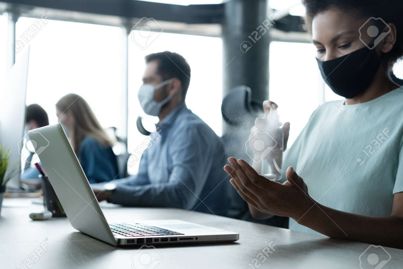 Portrait of young businesspeople with face masks working indoors in office, disinfecting laptop - 171828395 Portrait of young businesspeople with face masks working indoors in office, disinfecting laptop - 171828395
