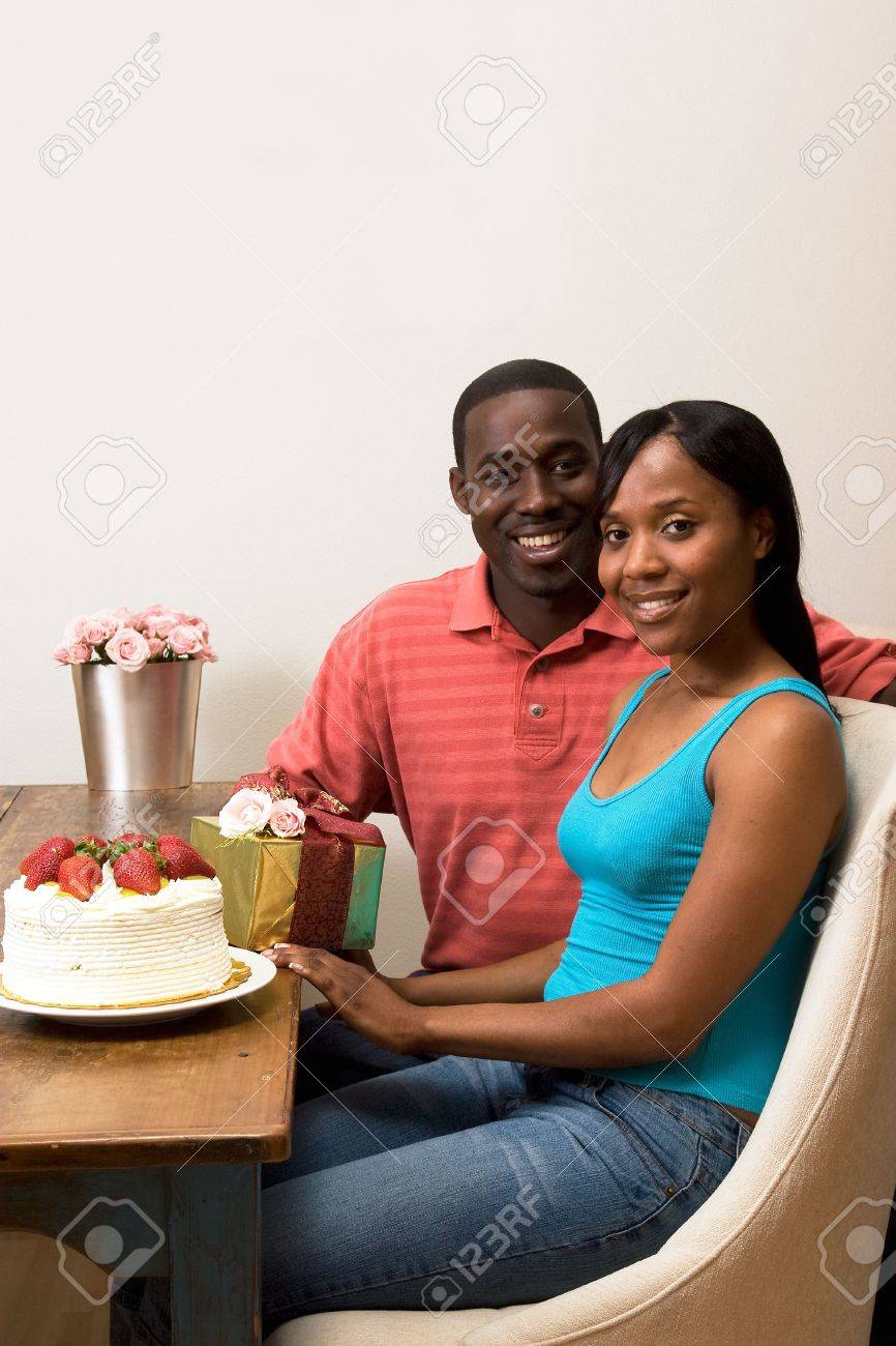 Tres Beau Couple Souriant Celebrer Un Anniversaire Assis A Une Table Le Haut Du Tableau Est Un Gateau Avec Le Givrage Des Fraises Un Cadeau Enveloppe Et De Fleurs Dans Le Cadre