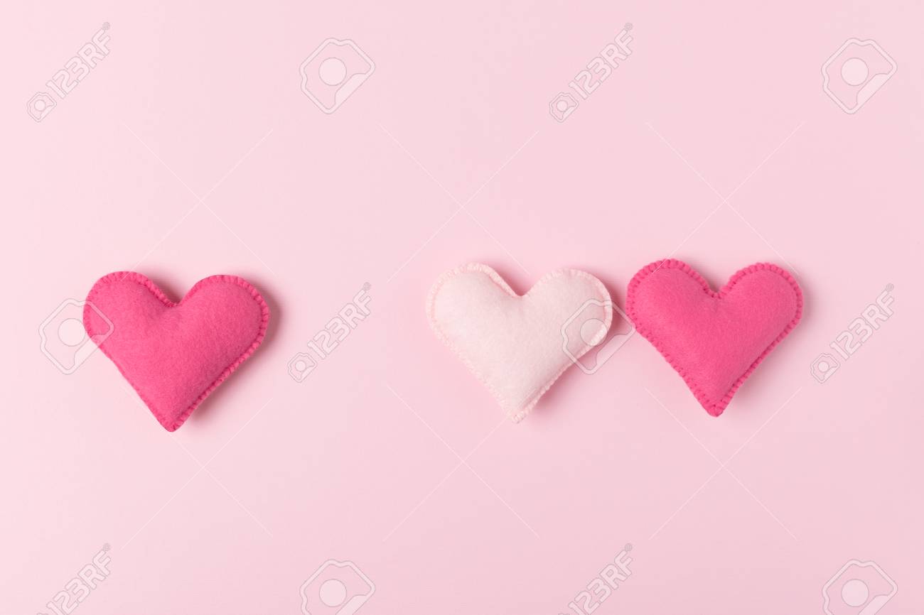 Three Hand Made Felt Hearts On Pastel Pink Background For Love