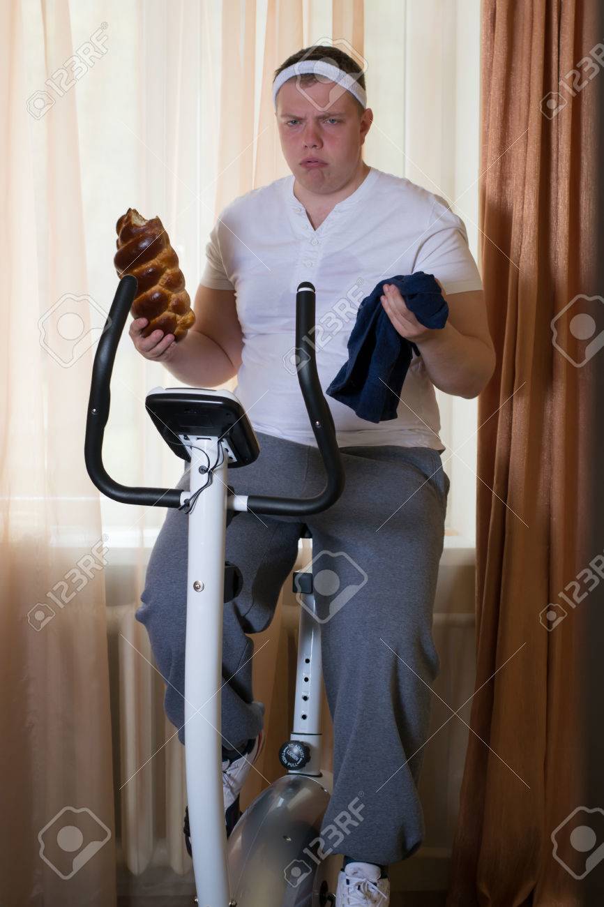 静止トレーニング自転車運動とパンを家で食べる脂肪の男 の写真素材 画像素材 Image