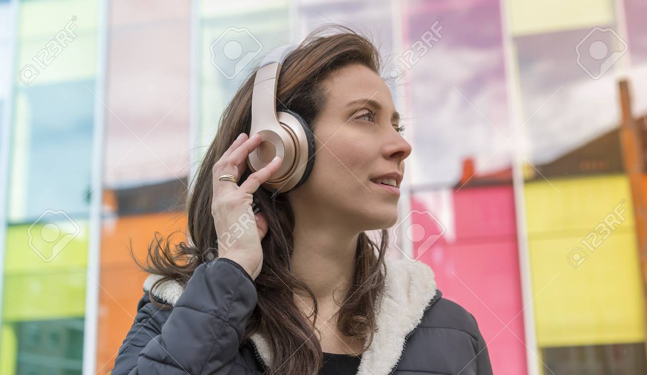 彼女の頭の上にヘッドフォンで音楽を聴いて通りの女の子は 彼女は風と冬のジャケットに長い髪を身に着けている の写真素材 画像素材 Image
