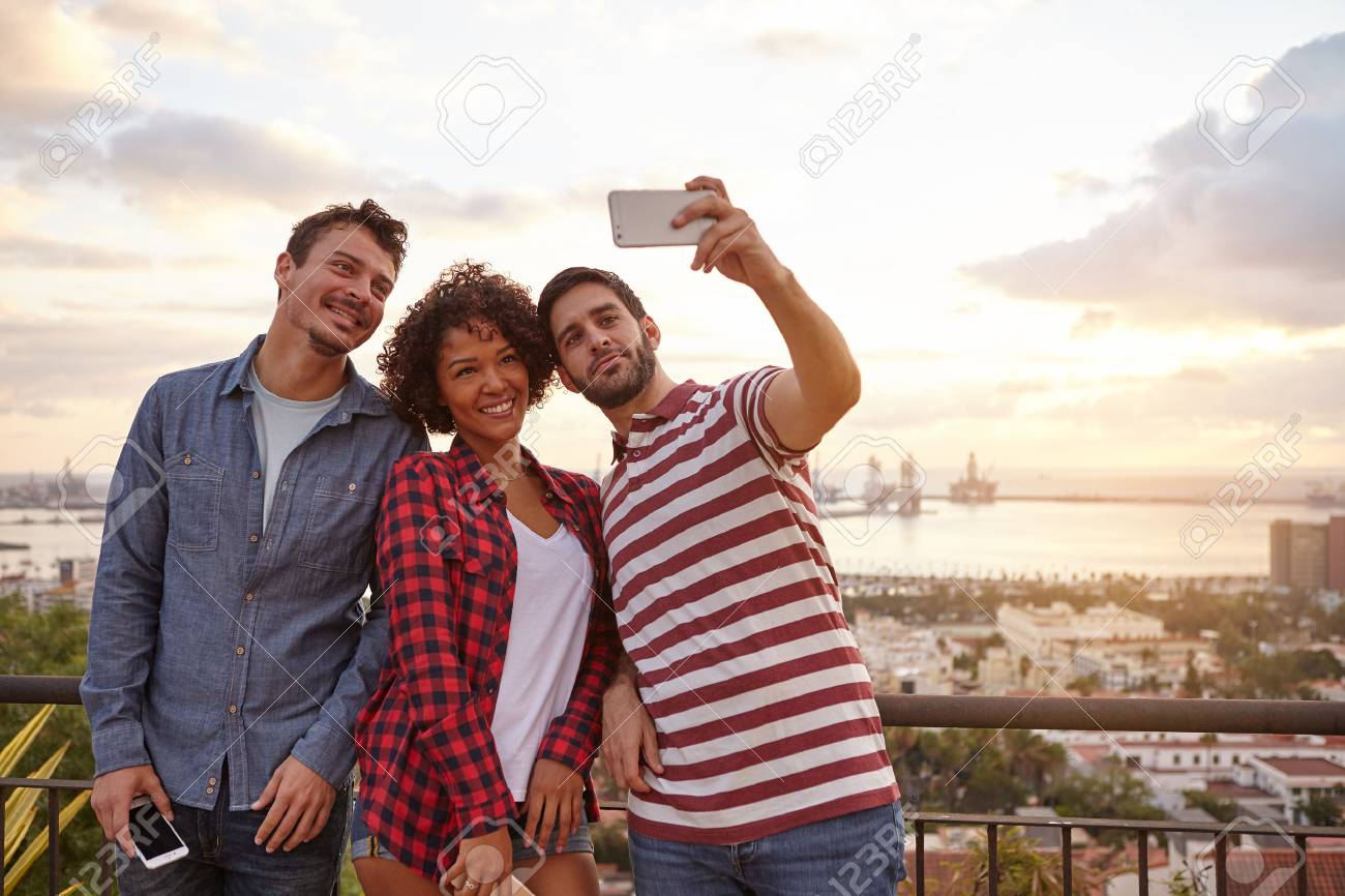 Tres Jovens Felizes Em Uma Ponte Que Leva Selfies Com Uma Cidade E Um Lago Atras Deles Enquanto Usam Roupas Casuais Fotos Retratos Imagenes Y Fotografia De Archivo Libres De Derecho Image