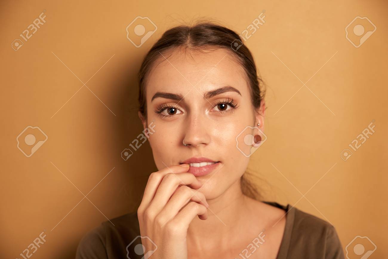 彼女の口に 笑顔と彼女の右手でカメラを見て 若い女性を思いやりのある 彼女の頭とカメラのためにポーズ の写真素材 画像素材 Image