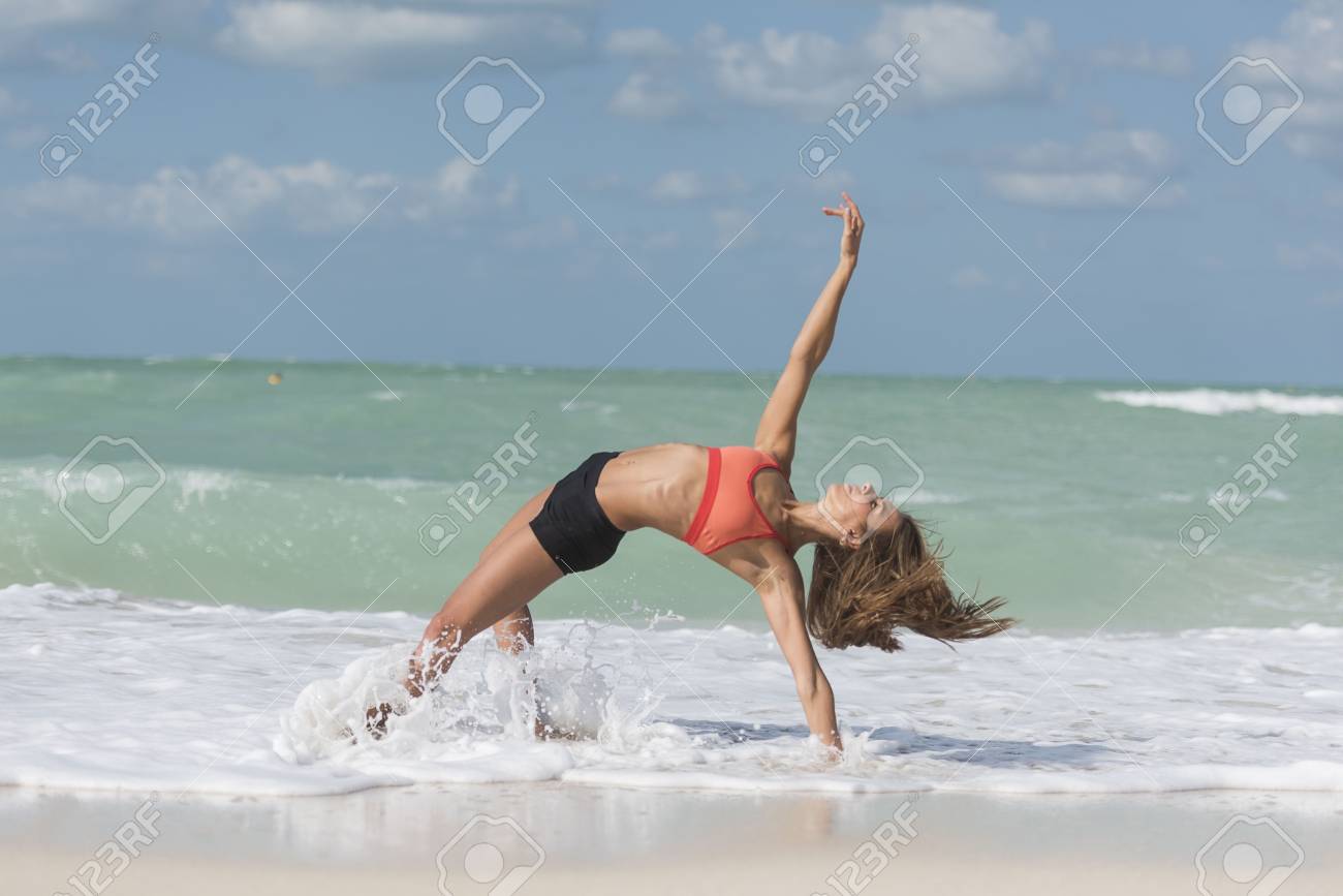 Beautiful Girl In Yoga Pose With Waves Splashing On Her On Beach Wearing  Sports Bra And Black Shorts Stock Photo, Picture and Royalty Free Image.  Image 98130963.