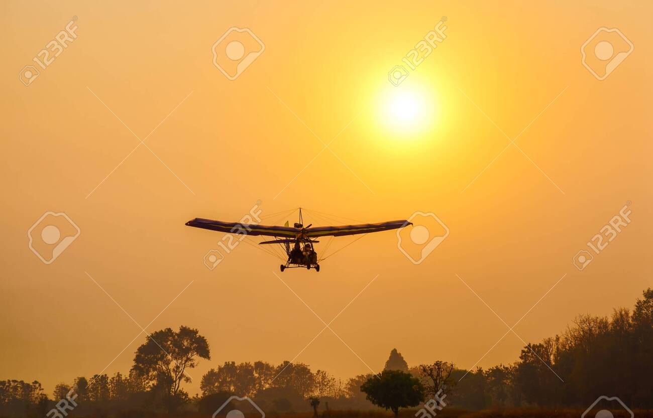Ultralight trike flying with a pilot and a passenger against sunset sky, A microlight aircraft with two passengers with the sun - 141181297 Ultralight trike flying with a pilot and a passenger against sunset sky, A microlight aircraft with two passengers with the sun - 141181297
