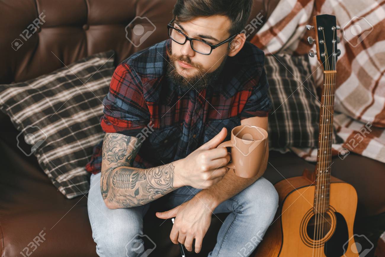 Young Guitarist Hipster At Home With Guitar Rest Drinking Tea Stock Photo,  Picture And Royalty Free Image. Image 93869688.