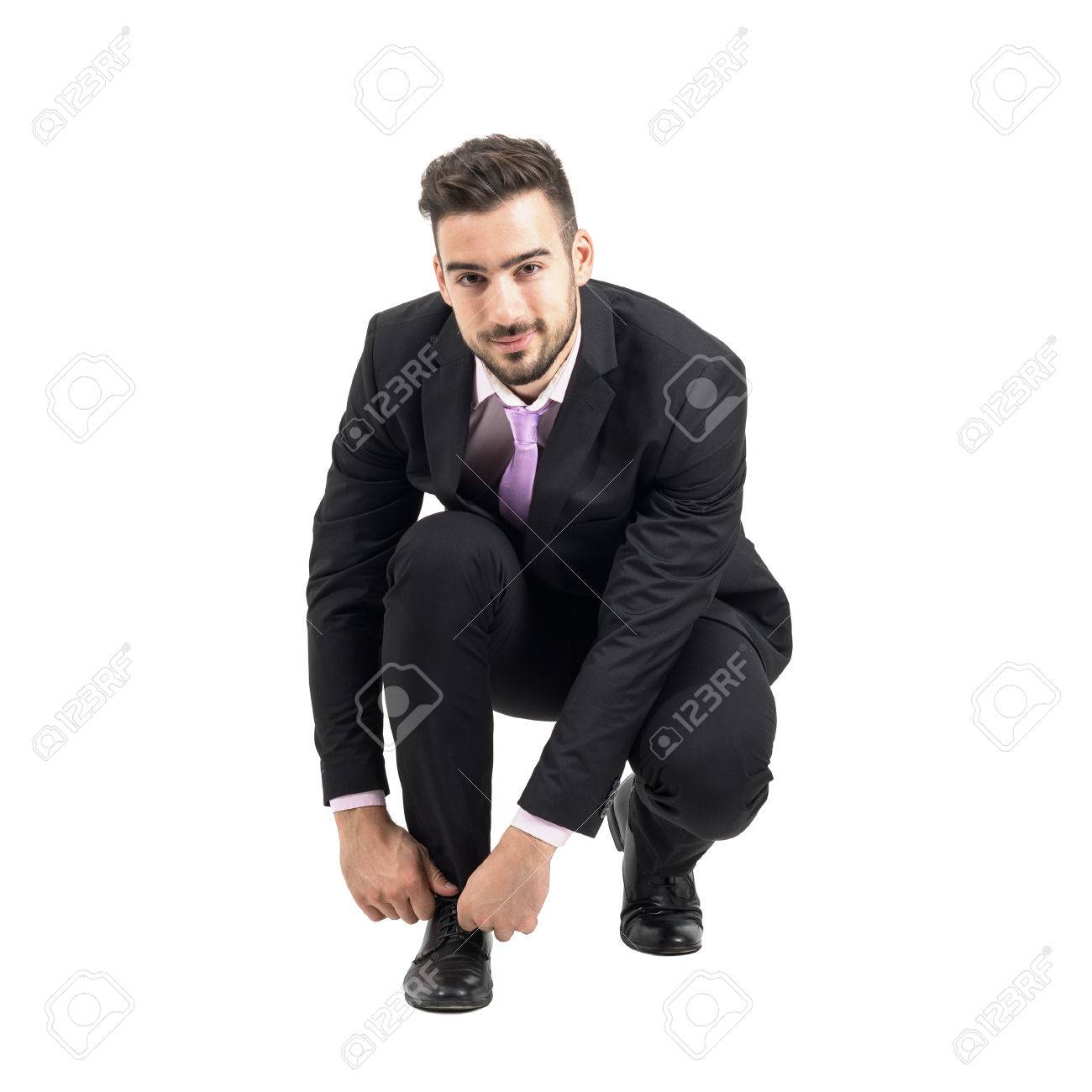 しゃがんでカメラを見て靴ひもを結ぶ青年実業家 フルボディの長さの肖像画は 白いスタジオ背景に分離されました の写真素材 画像素材 Image