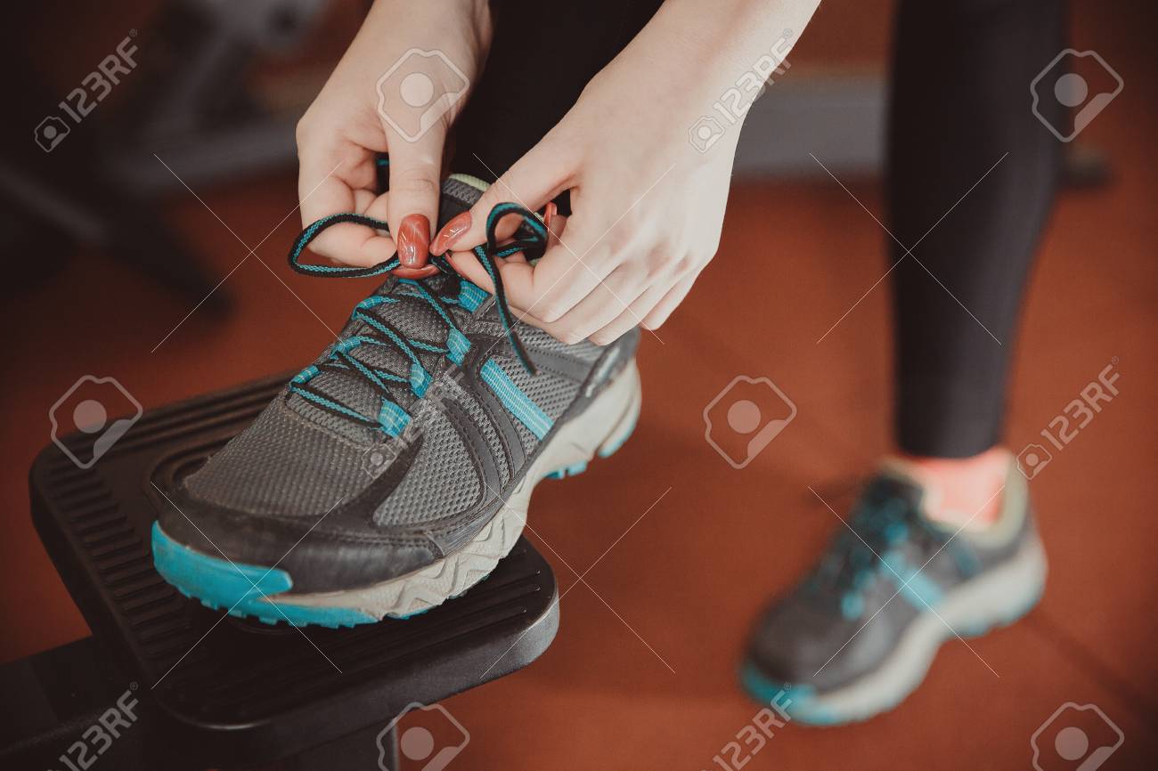 Close Up Of Girl Tying Shoelaces On Sports Shoes In Gym Stock