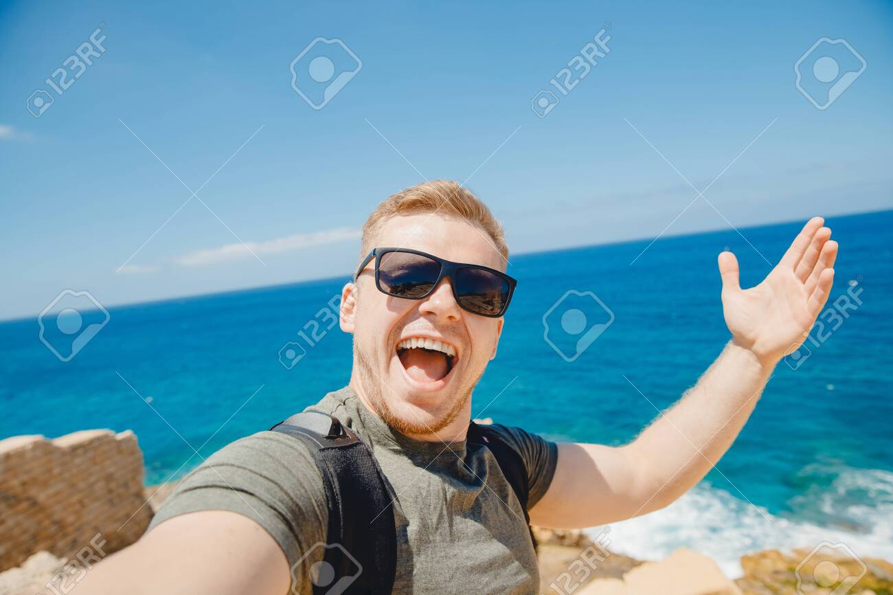 Happy traveler man taking selfie photo in sunglasses on background of bruise sea with backpack. Travel concept - 140261739 Happy traveler man taking selfie photo in sunglasses on background of bruise sea with backpack. Travel concept - 140261739