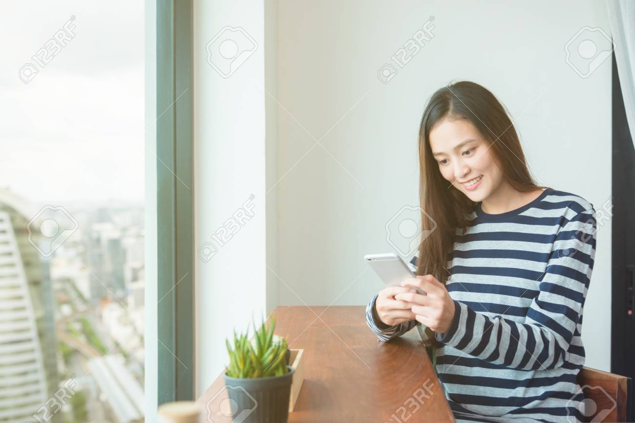Beautiful asian woman reading message on mobile phone and smiles - 90773295 Beautiful asian woman reading message on mobile phone and smiles - 90773295