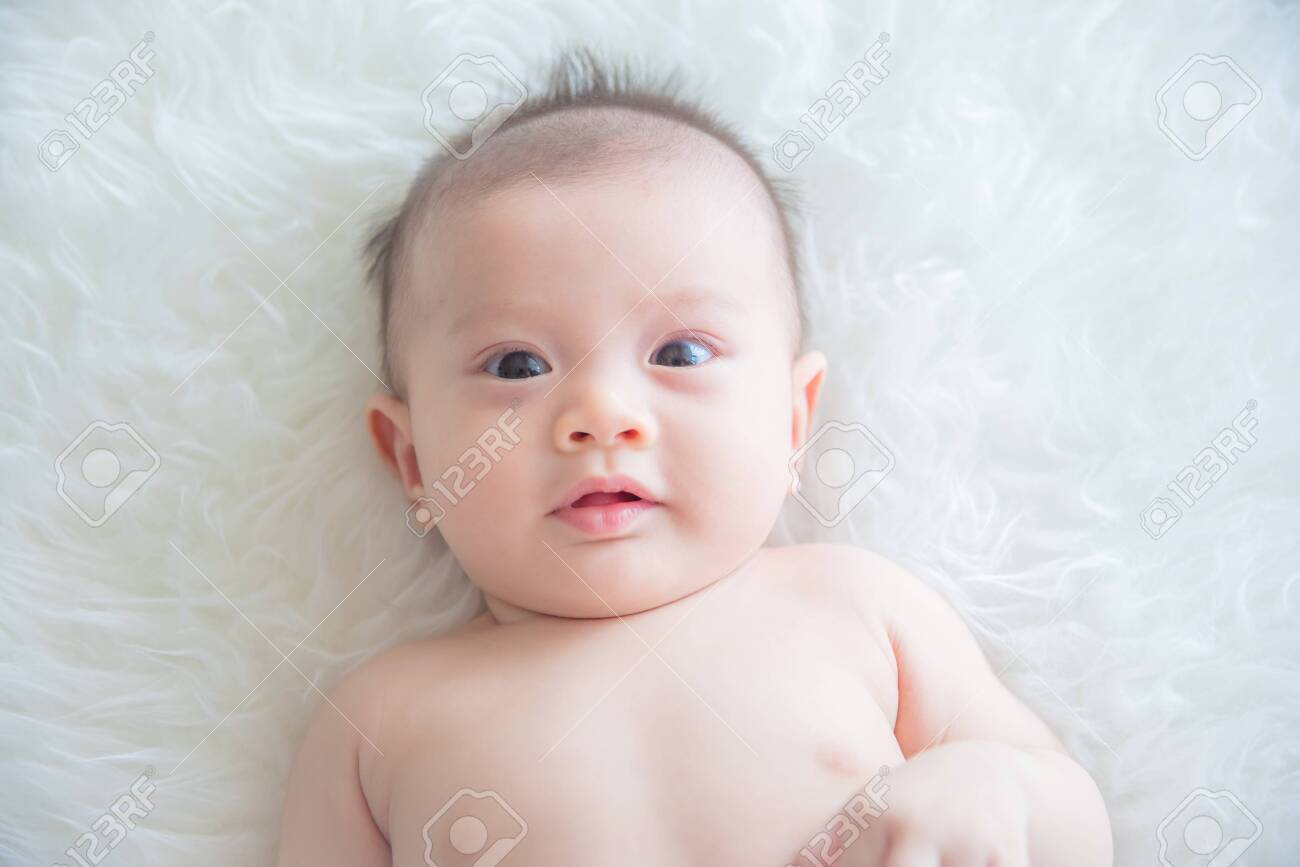 Little asian baby lying on bed and looking at camera - 123955020 Little asian baby lying on bed and looking at camera - 123955020