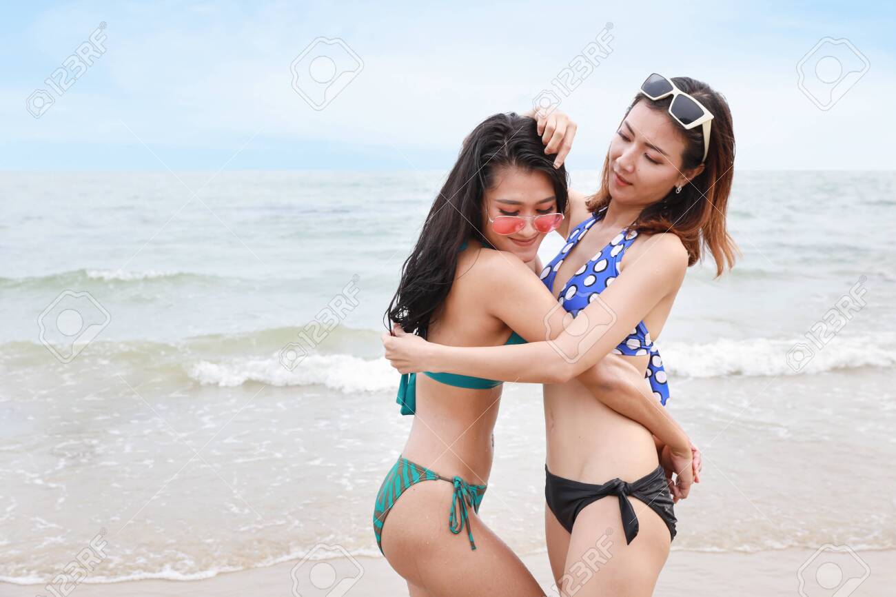 Two Beauty And Sexy Asian Lesbian Women In Green And Blue Bikini Who Standing And Embracing On Sandy Beach And They Looking At Camera Stock Photo, Picture and Royalty Free Image picture