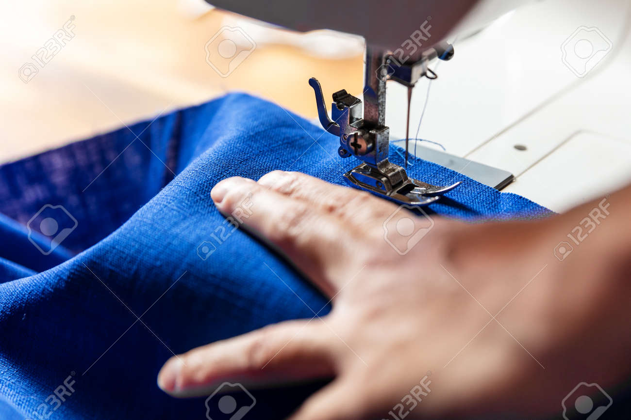 hand of a woman is working with blue linen on a sewing machine - 170381919 hand of a woman is working with blue linen on a sewing machine - 170381919