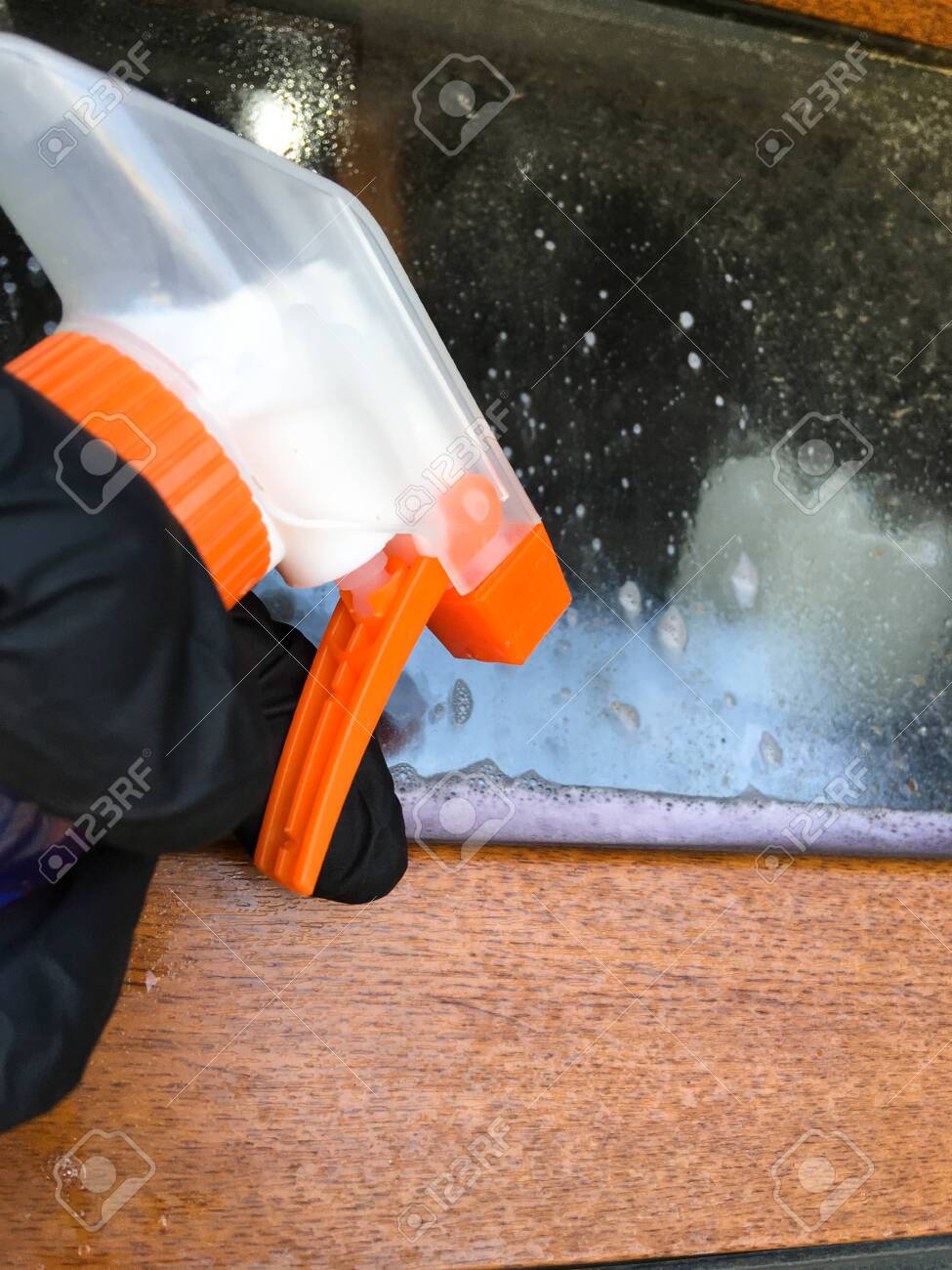 A woman in a black glove cleans a window with a spray bottle. House cleaning. Washing dirty window detergents in summer. - 149039771 A woman in a black glove cleans a window with a spray bottle. House cleaning. Washing dirty window detergents in summer. - 149039771