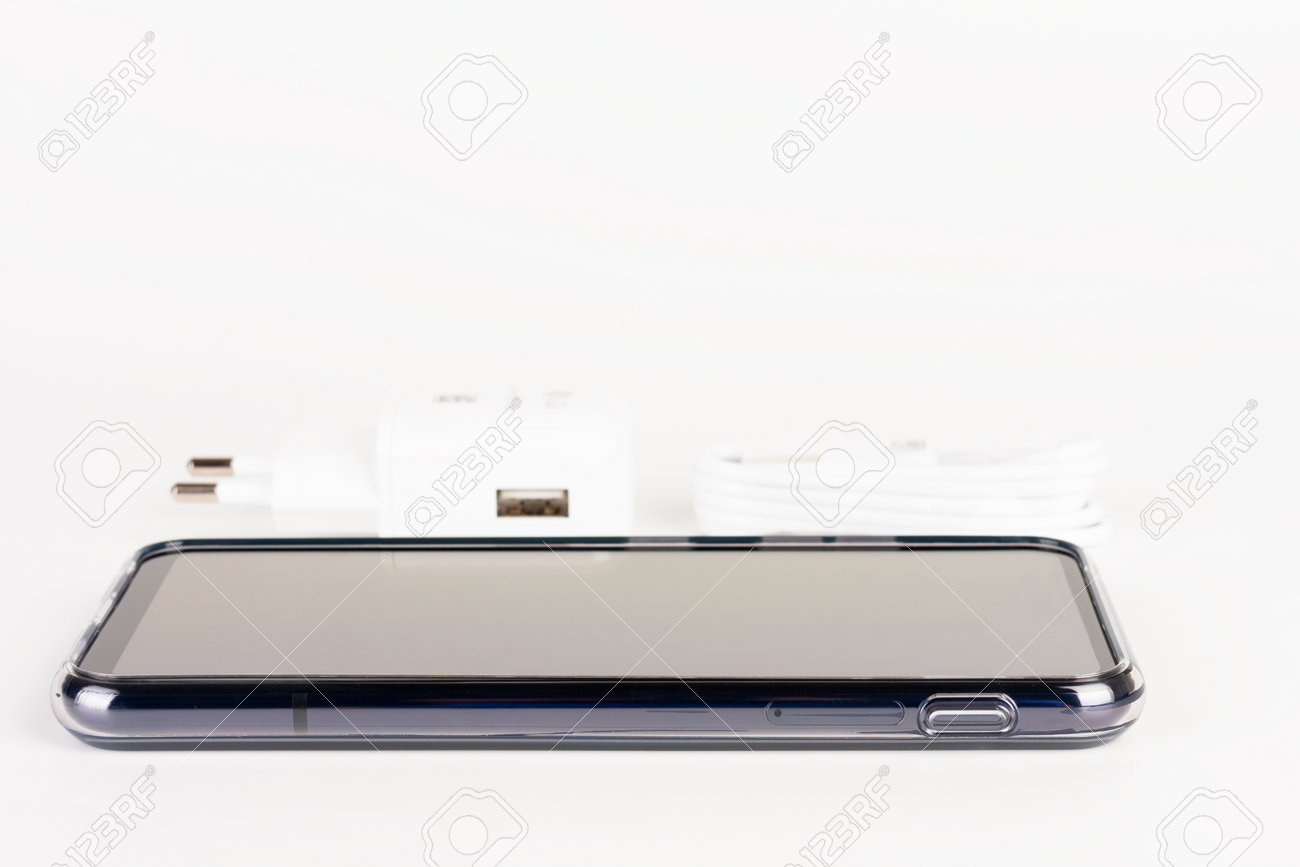 Touchscreen smartphone in silicone cover, charger in background. - 162659598 Touchscreen smartphone in silicone cover, charger in background. - 162659598