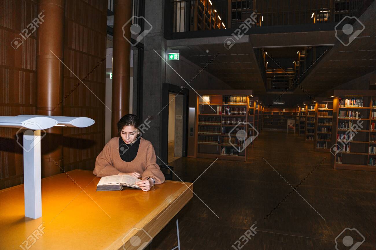 Girl reads book by light of lamp sitting at table - 132001829 Girl reads book by light of lamp sitting at table - 132001829