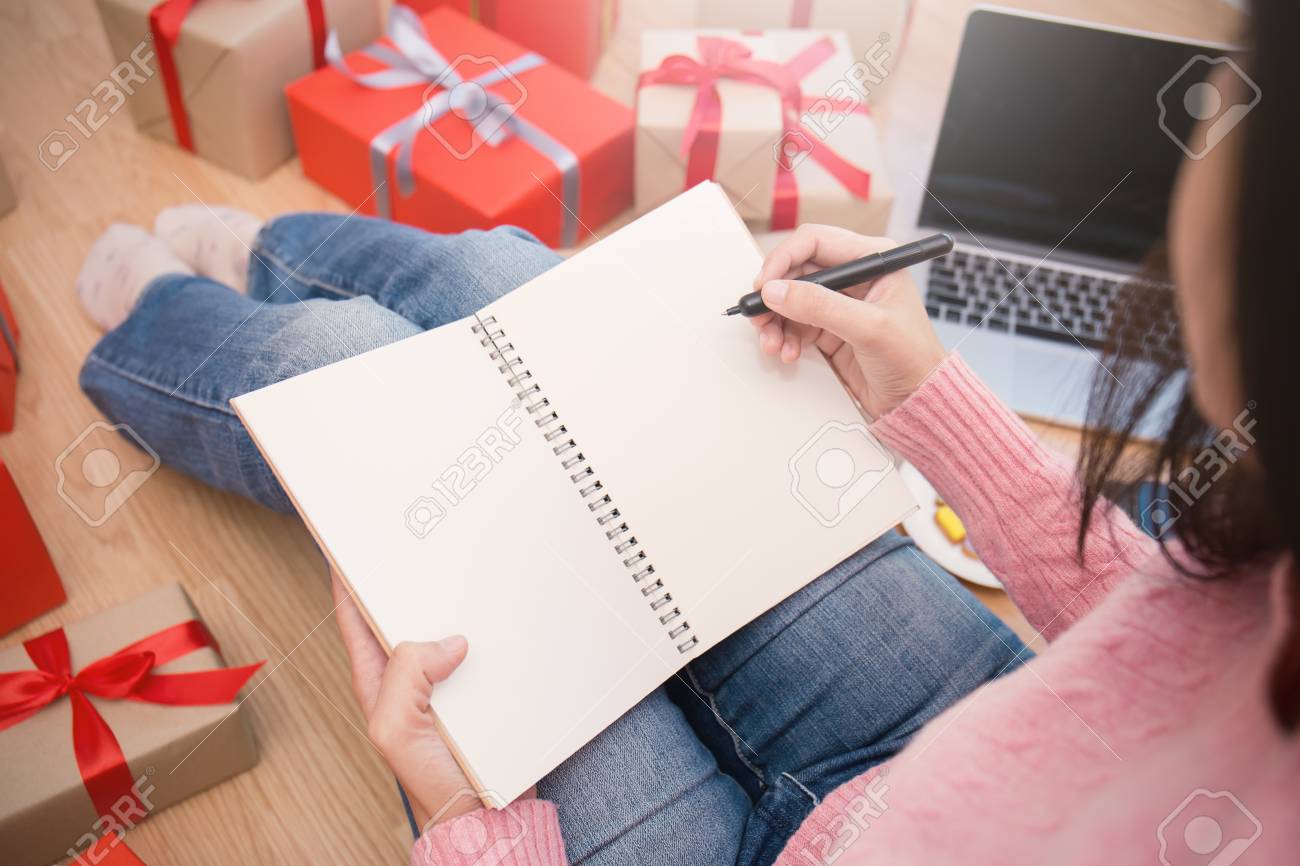 hands holding pen whiting on notebook making gift list with online christmas shopping list